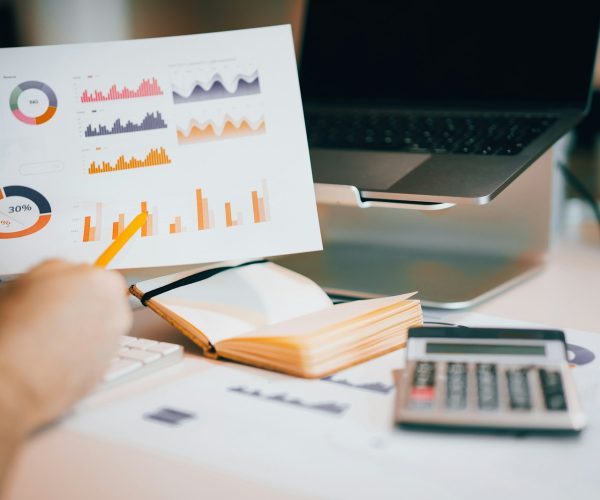 Financial charts, notebook, laptop, and calculator on a work desk